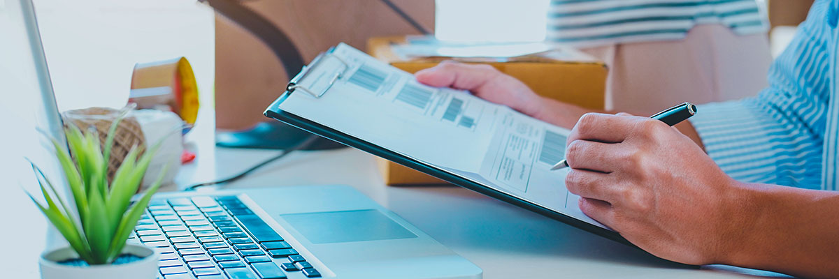 Homem em frente a um notebook, fazendo anotações em uma planilha