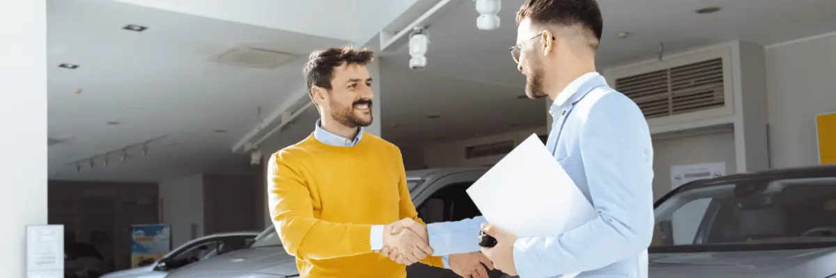 Dois homens, em uma concessionária de automóveis, apertando as mãos.